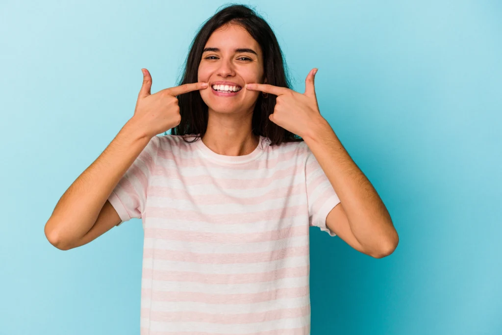 8 Summer Oral Health Tips to Keep Your Teeth Healthy 1 young caucasian woman isolated blue background smiles pointing fingers mouth 1